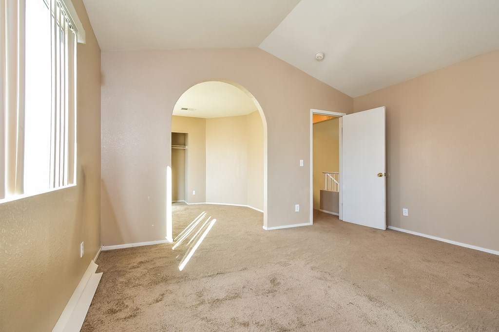 A spacious room with a carpeted floor and a large arched doorway leading to another room.