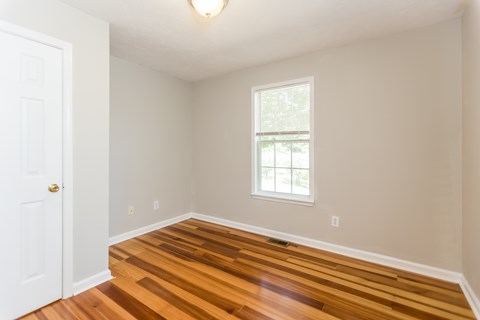 A room with a white door and a window with a wooden floor.