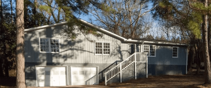 A grey house with a white garage door and a staircase leading to the garage.