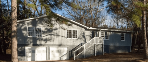 A grey house with a white garage door and a staircase leading to the garage.