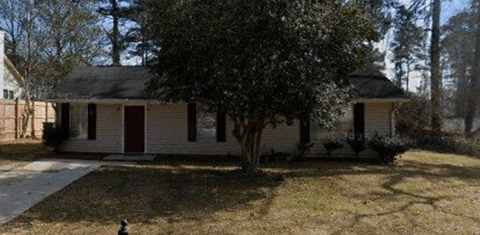 A small house with a red door is surrounded by trees.