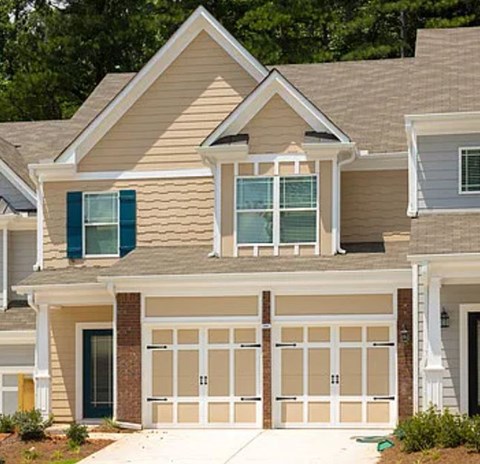 A two-story house with a garage door and a window with blue shutters.
