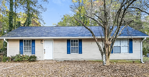 A house with a blue roof and white walls with a tree in front.