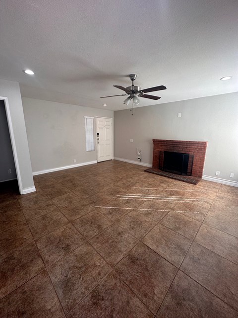 an empty living room with a brick fireplace and a ceiling fan