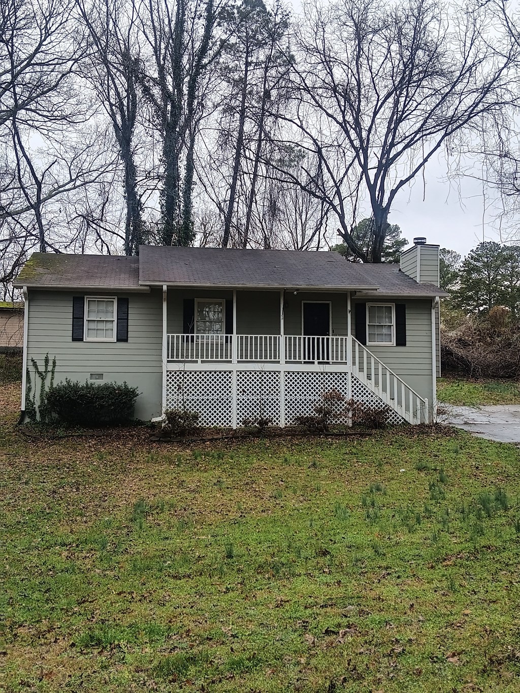 A small house with a porch and a tree in the background.