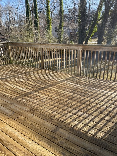 A wooden deck with a railing and trees in the background.