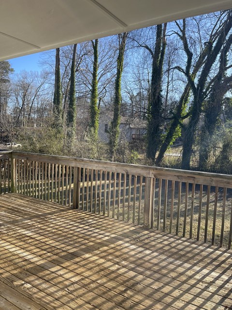 A wooden deck with a railing overlooking a wooded area.