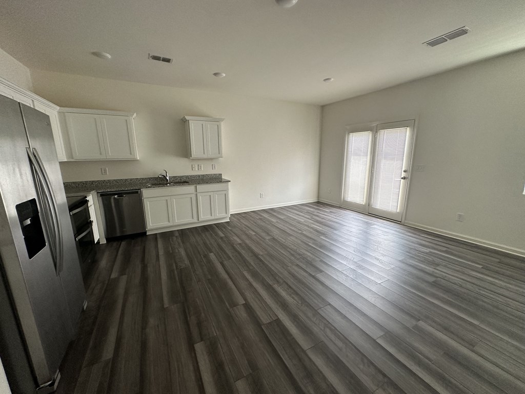 an empty kitchen and living room with wooden floors and white cabinets