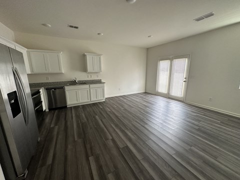 an empty kitchen and living room with wooden floors and white cabinets