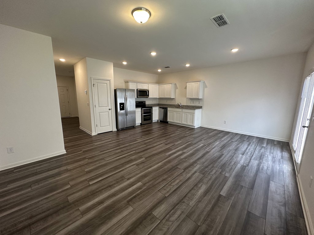an empty living room and kitchen with wood flooring