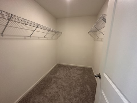 an empty bedroom with a closet and a wire shelf on the wall