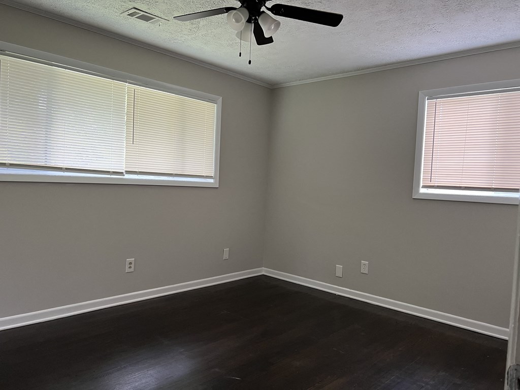 an empty bedroom with a ceiling fan and two windows