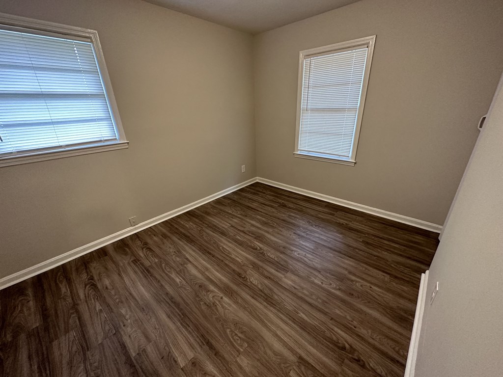 A room with wooden flooring and two windows.