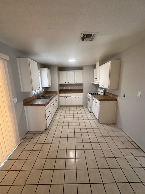 an empty kitchen with white cabinets and tiled floors