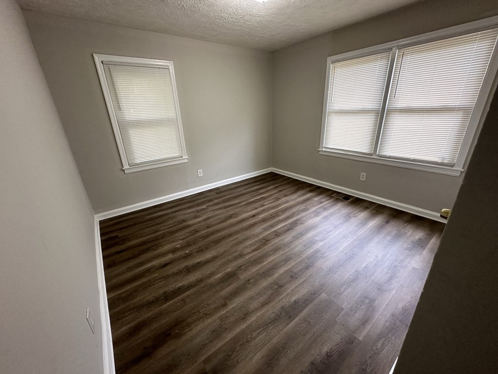 an empty room with wooden floors and two windows
