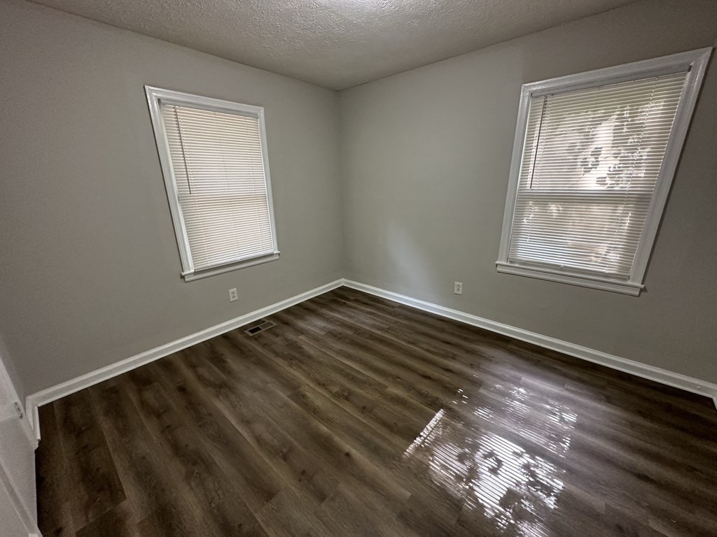 an empty room with wooden floors and two windows