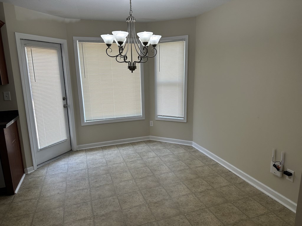 an empty dining room with two windows and a chandelier