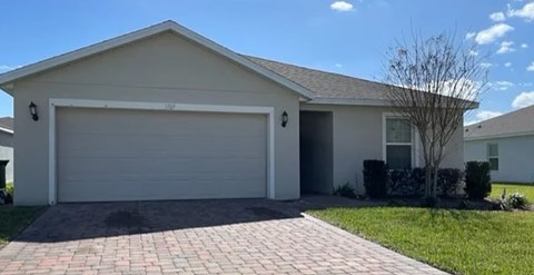 A house with a grey garage door and a brick driveway.