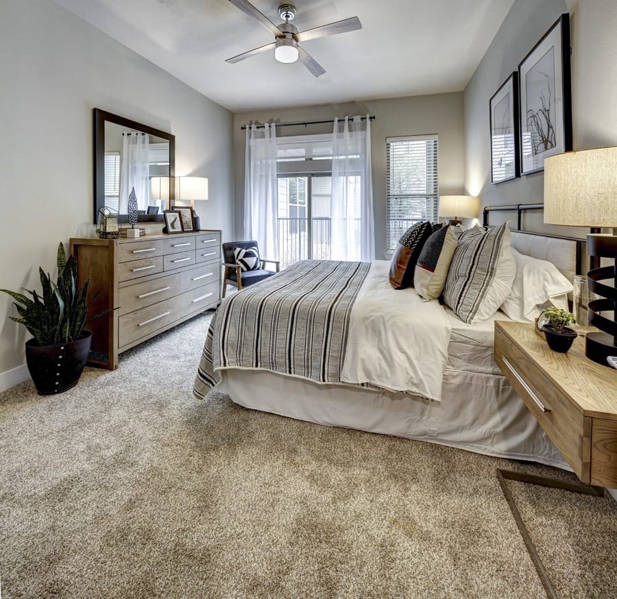 A bedroom with a large bed, a dresser, and a ceiling fan at Arise Riverside Apartments, Austin