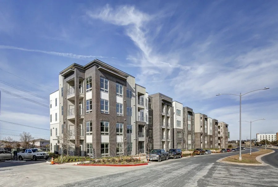 A row of modern apartment buildings with cars parked in front at Arise Riverside Apartments, Austin, TX, 78741