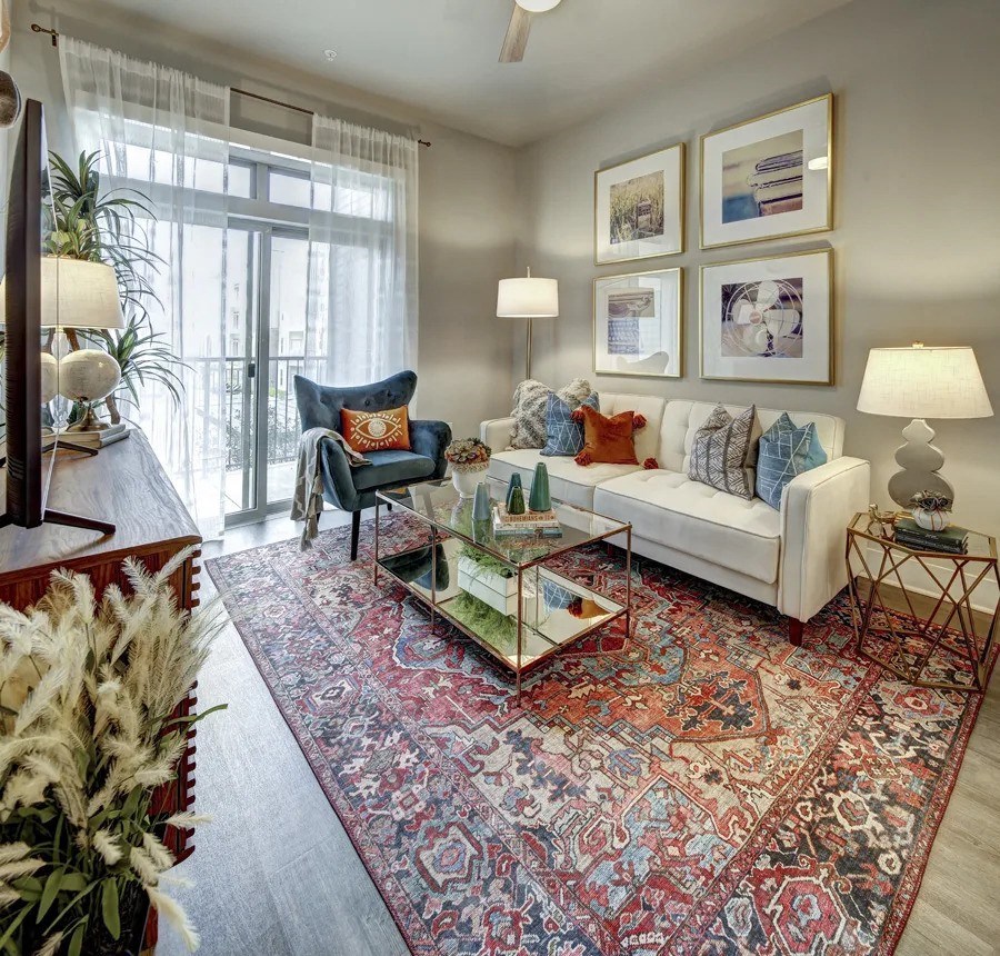 A living room with a white couch, a blue chair, and a large rug at Arise Riverside Apartments, Austin, TX, 78741
