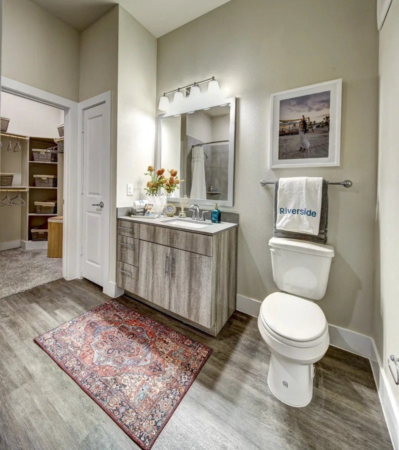 A bathroom with a rug on the floor and a toilet next to a sink at Arise Riverside Apartments, Austin, TX, 78741