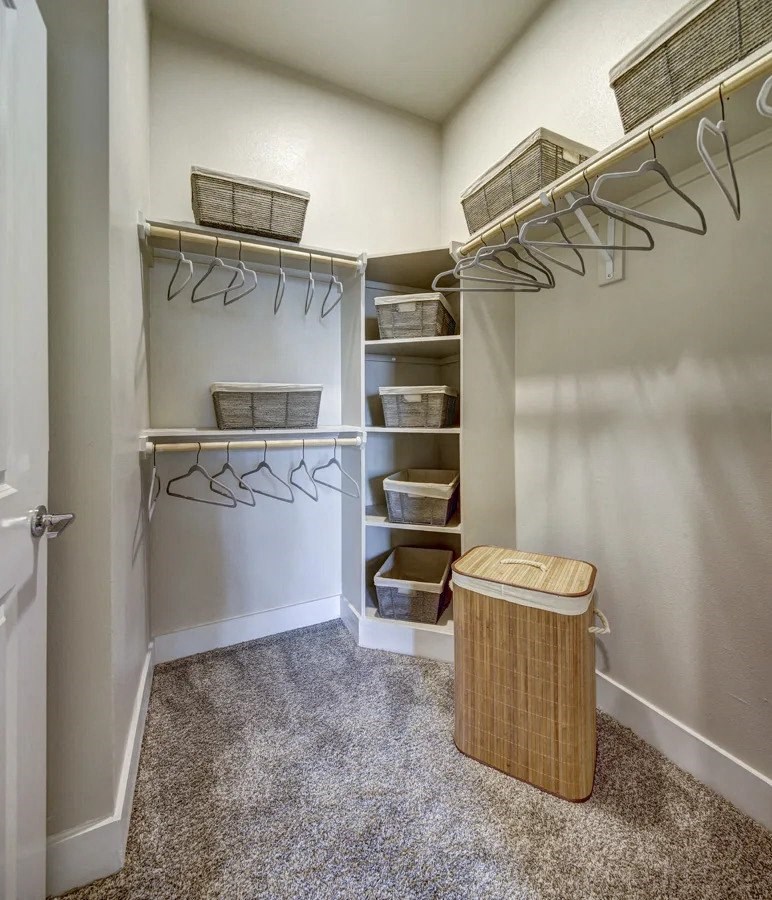 A white closet with a carpeted floor and a trash can at Arise Riverside Apartments, Austin, TX
