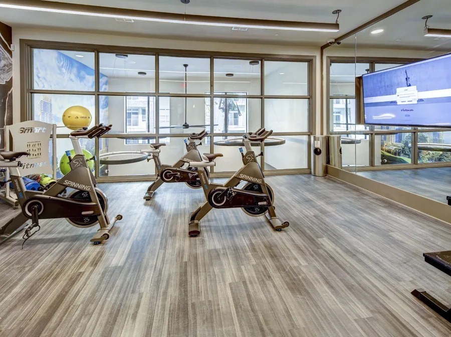 A room with exercise bikes and a TV screen at Arise Riverside Apartments, Texas