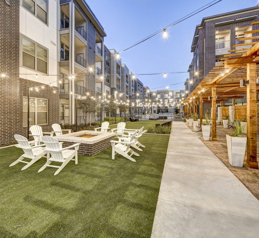 A patio with white chairs and a table is surrounded by apartment buildings at Arise Riverside Apartments, Austin, TX, 78741