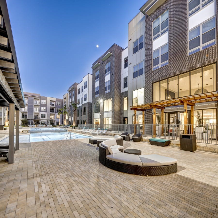 A modern outdoor pool area with a wooden deck and lounge chairs at Arise Riverside Apartments, Texas
