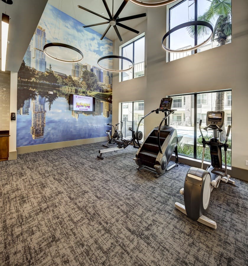 A gym with exercise equipment and a wall mural at Arise Riverside Apartments, Austin, 78741