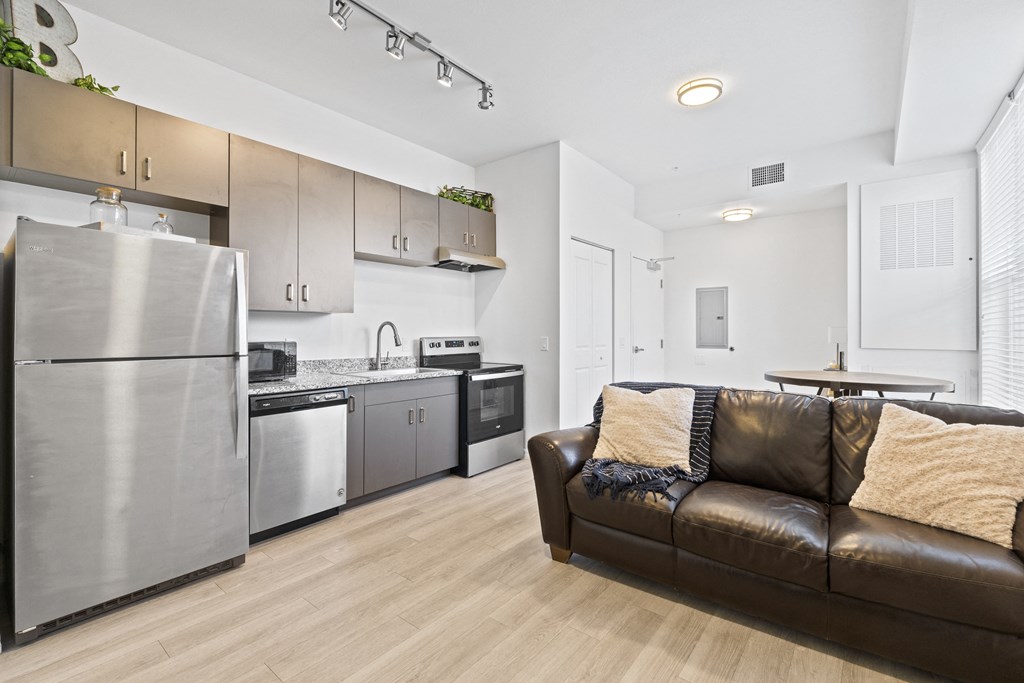 a living room with a leather couch and a kitchen with stainless steel appliances