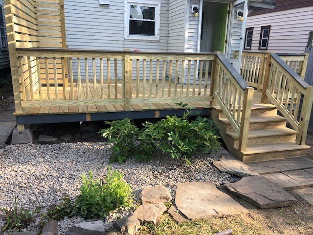 a porch with a wooden deck and a white house in the background