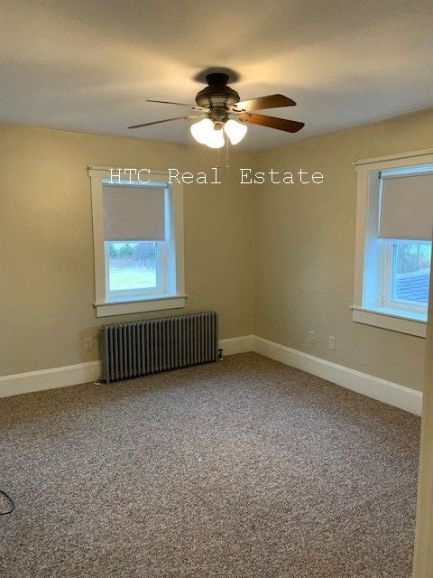 A room with a carpet floor, a ceiling fan, and a window with blinds.