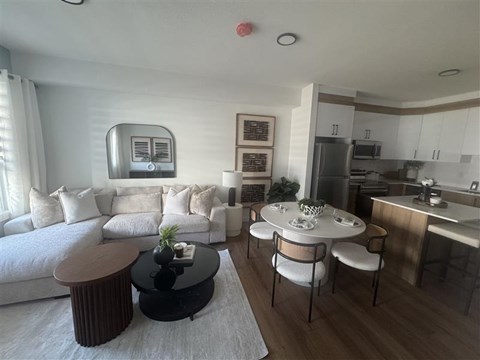 A modern living room with a white sofa, a black coffee table, and a dining area with a white table and chairs.
