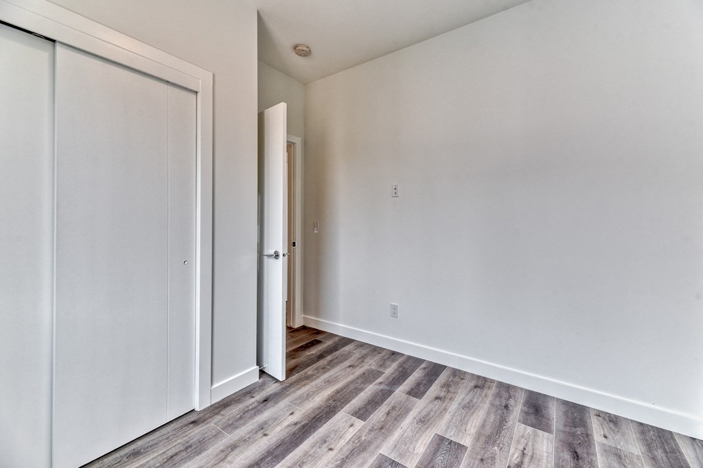 A room with a white door and a grey wood floor.