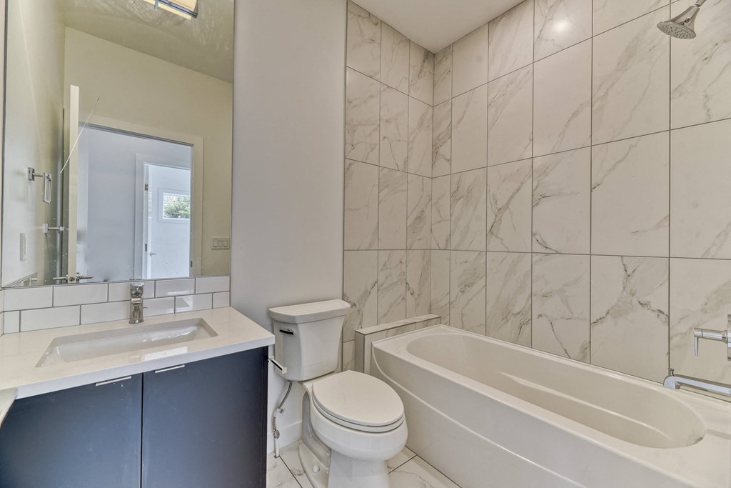 A white toilet sits next to a bathtub in a bathroom with marble tiles.