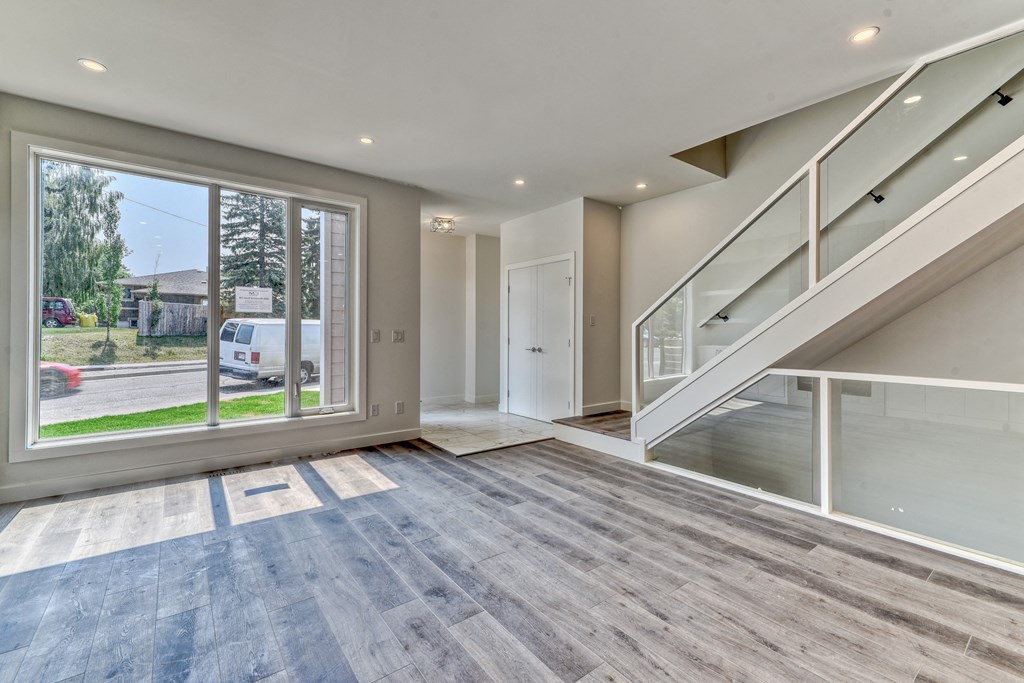 A spacious room with a staircase and a large window overlooking a street.
