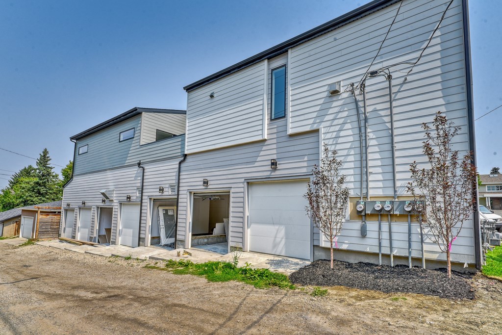 A large grey building with a garage door open and a tree in front.