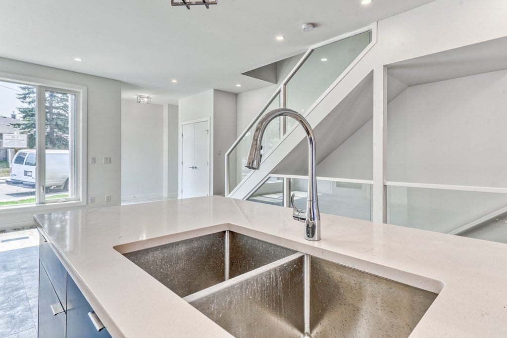 A modern kitchen with a stainless steel sink and a glass staircase.
