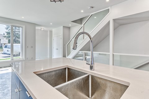 A modern kitchen with a stainless steel sink and a glass staircase.