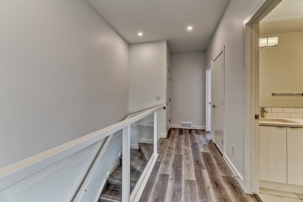 A hallway with a staircase and a bathroom visible in the distance.