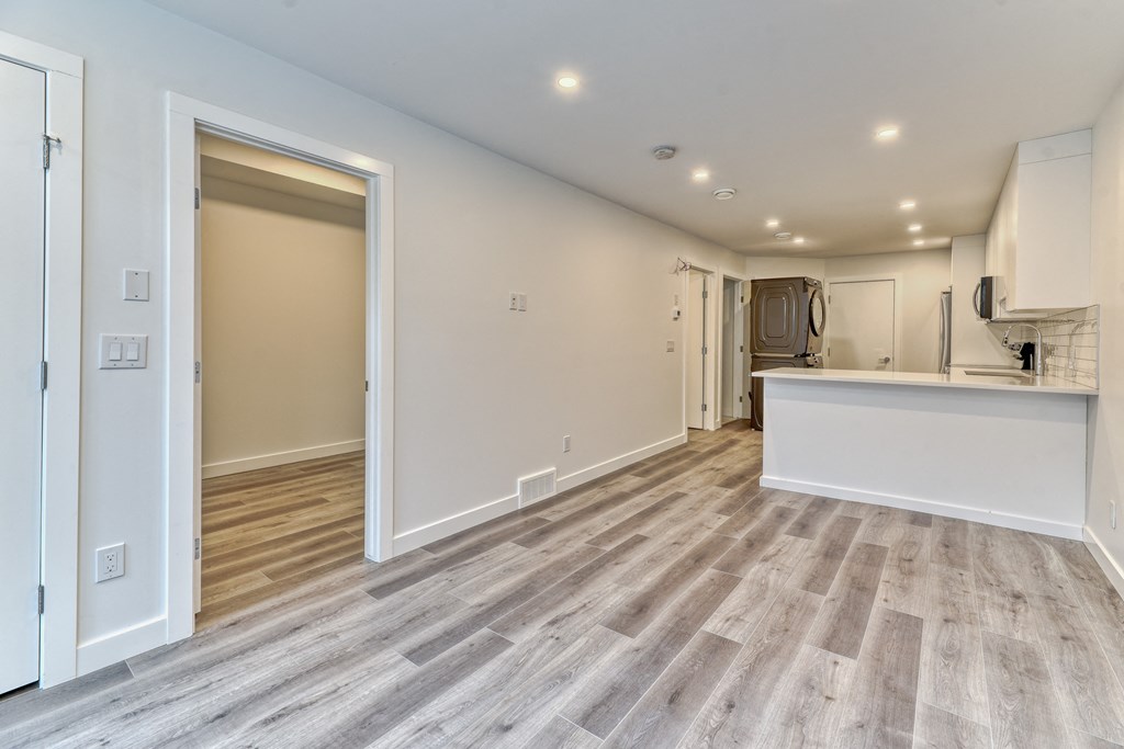 A spacious room with wooden flooring and a kitchen area in the background.