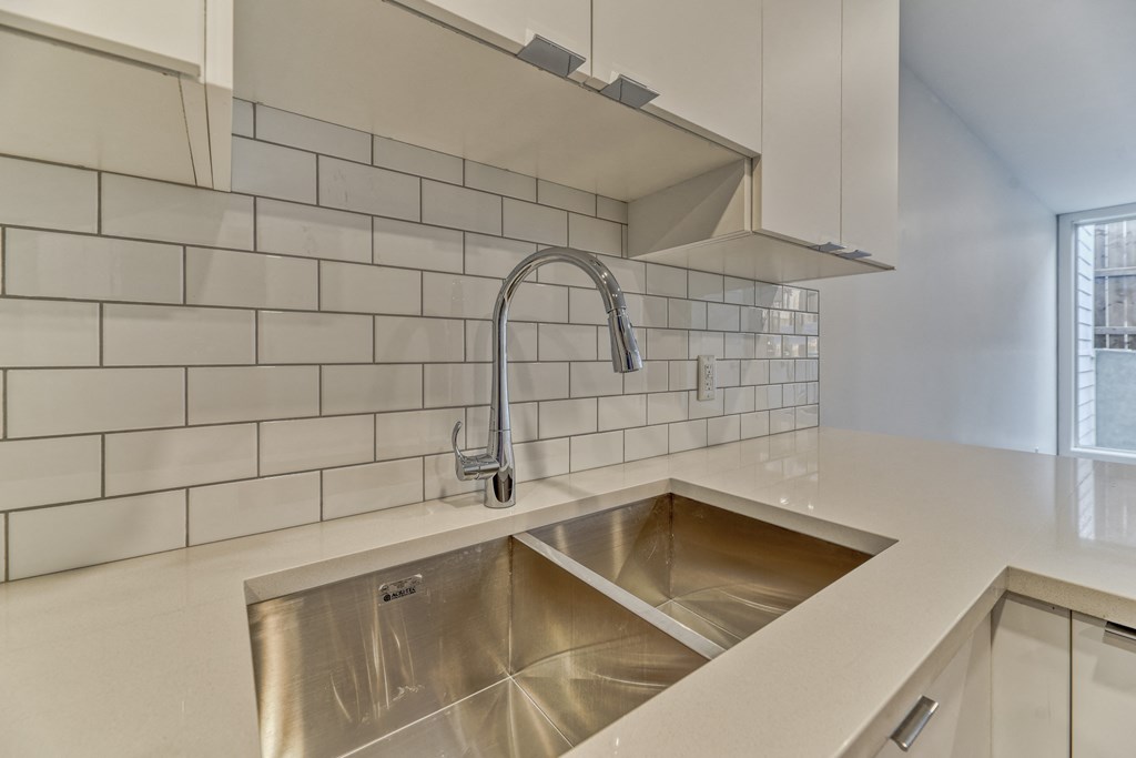 A modern kitchen with a stainless steel sink and white tiled backsplash.