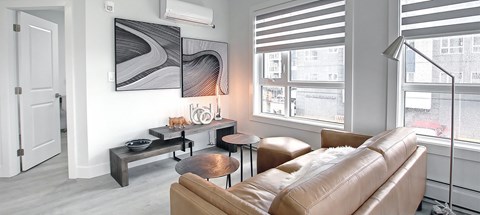 A living room with a brown leather couch, a black and white abstract painting on the wall, and a window with blinds.