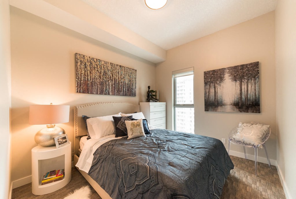 A bedroom with a bed, nightstand, and two pictures on the wall.