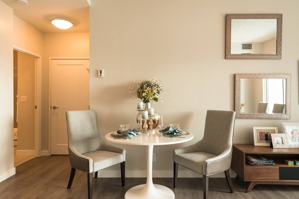 A dining room with a table set for two and a vase of flowers on the table.