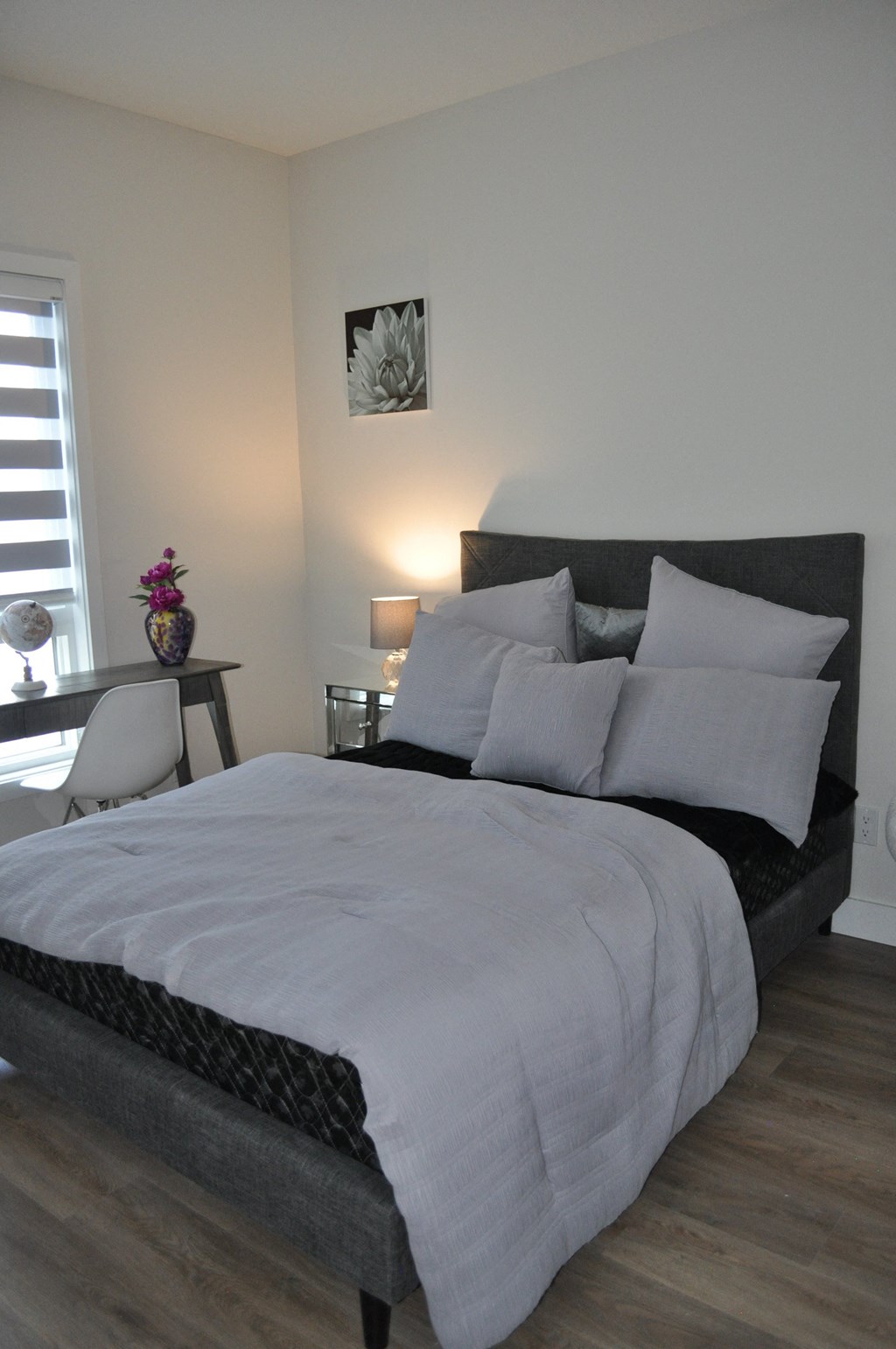 A bed with a white comforter and a black headboard with a picture of a flower on the wall at The Laurent at Laurel Apartments, Edmonton, AB