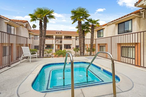 A pool surrounded by palm trees and a building in the background.