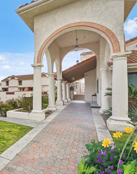 A white archway with a brick pathway leading to a building.